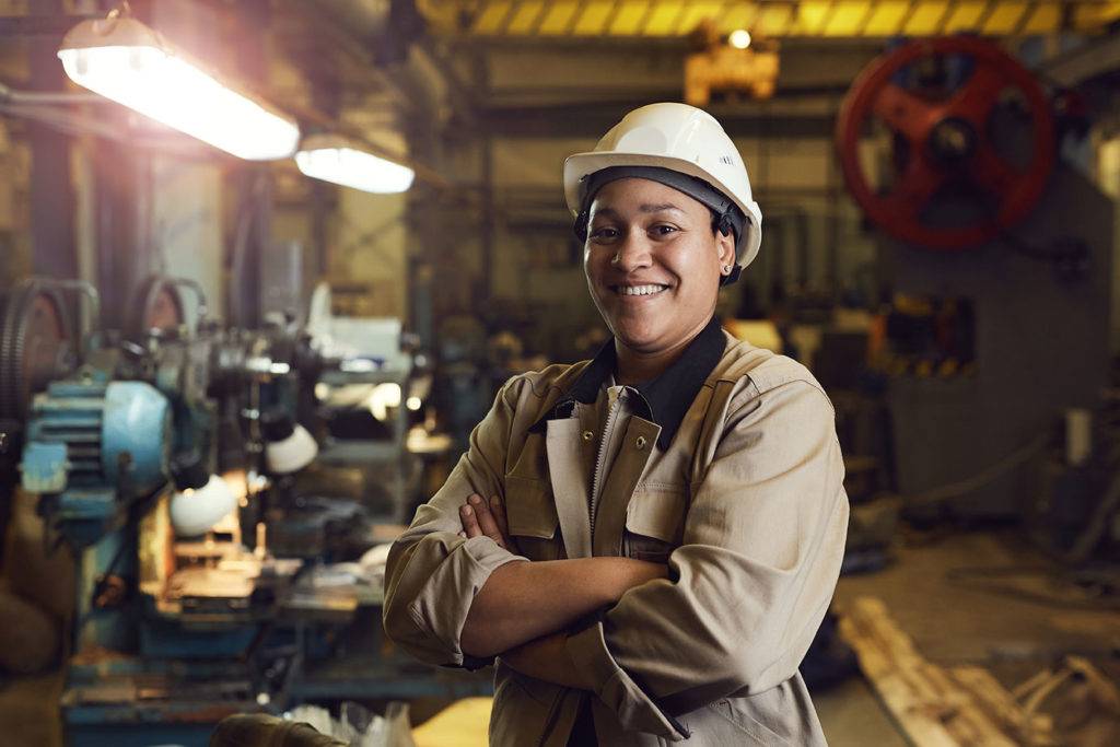 Portrait of female worker posing confidently while standing with arms crossed in factory workshop